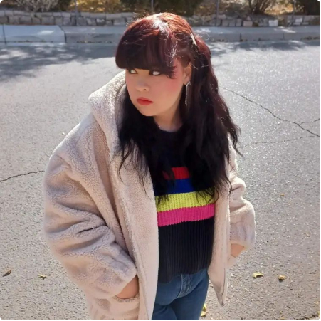 Young woman is shown outside wearing a pick jacket and colorful sweater