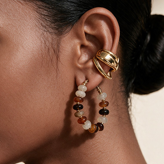 A close-up of multicolor beaded hoop earrings styled with a polished gold-tone wraparound ear cuff.